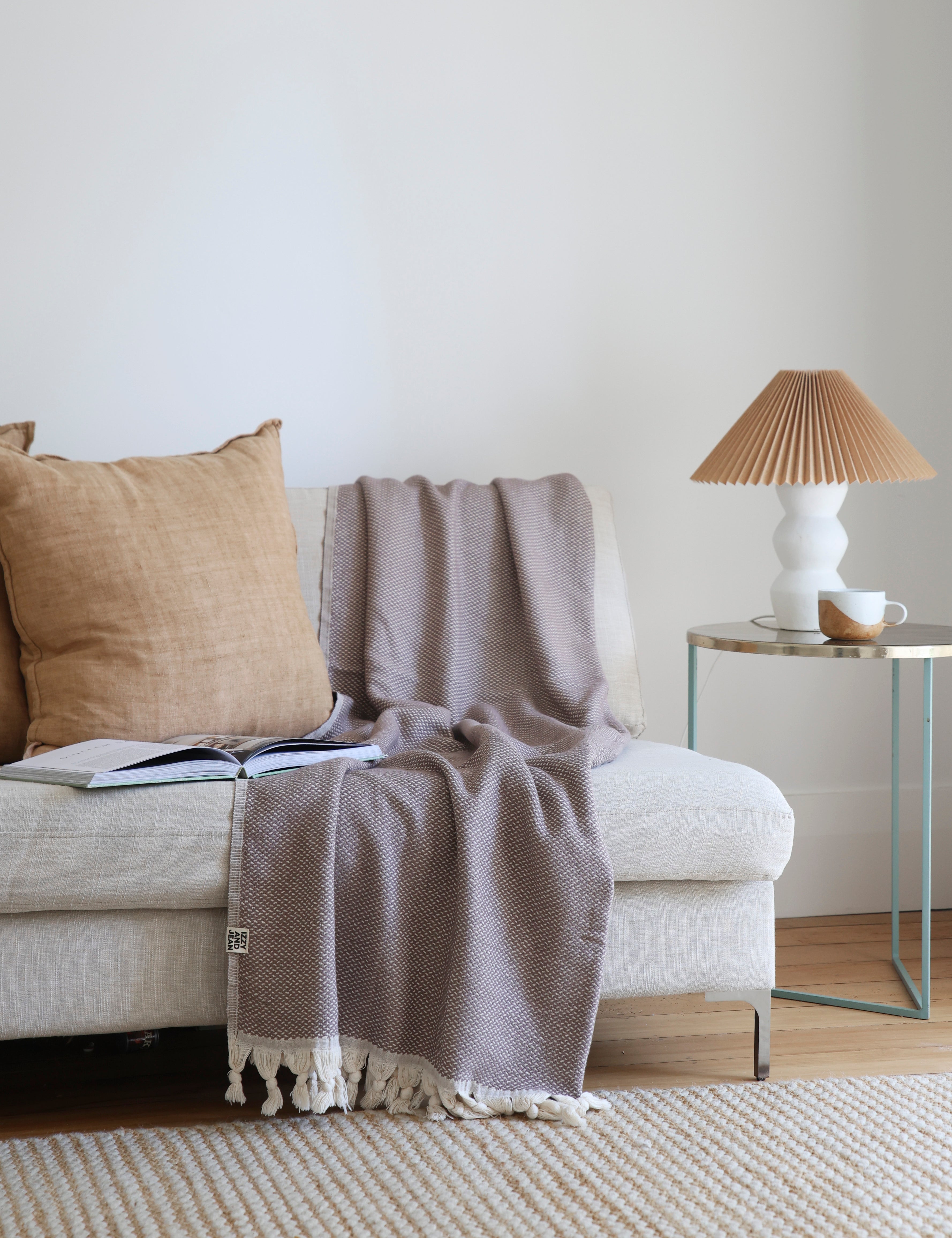 Brown throw blanket on a beige sofa with a lamp and coffee cup on a side table.