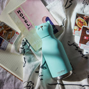 Turquoise cat-shaped water bottle on a bed with cards and a notebook.
