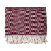A burgundy throw blanket made from 100% cotton, with a herringbone pattern and fringed edges on a white background.