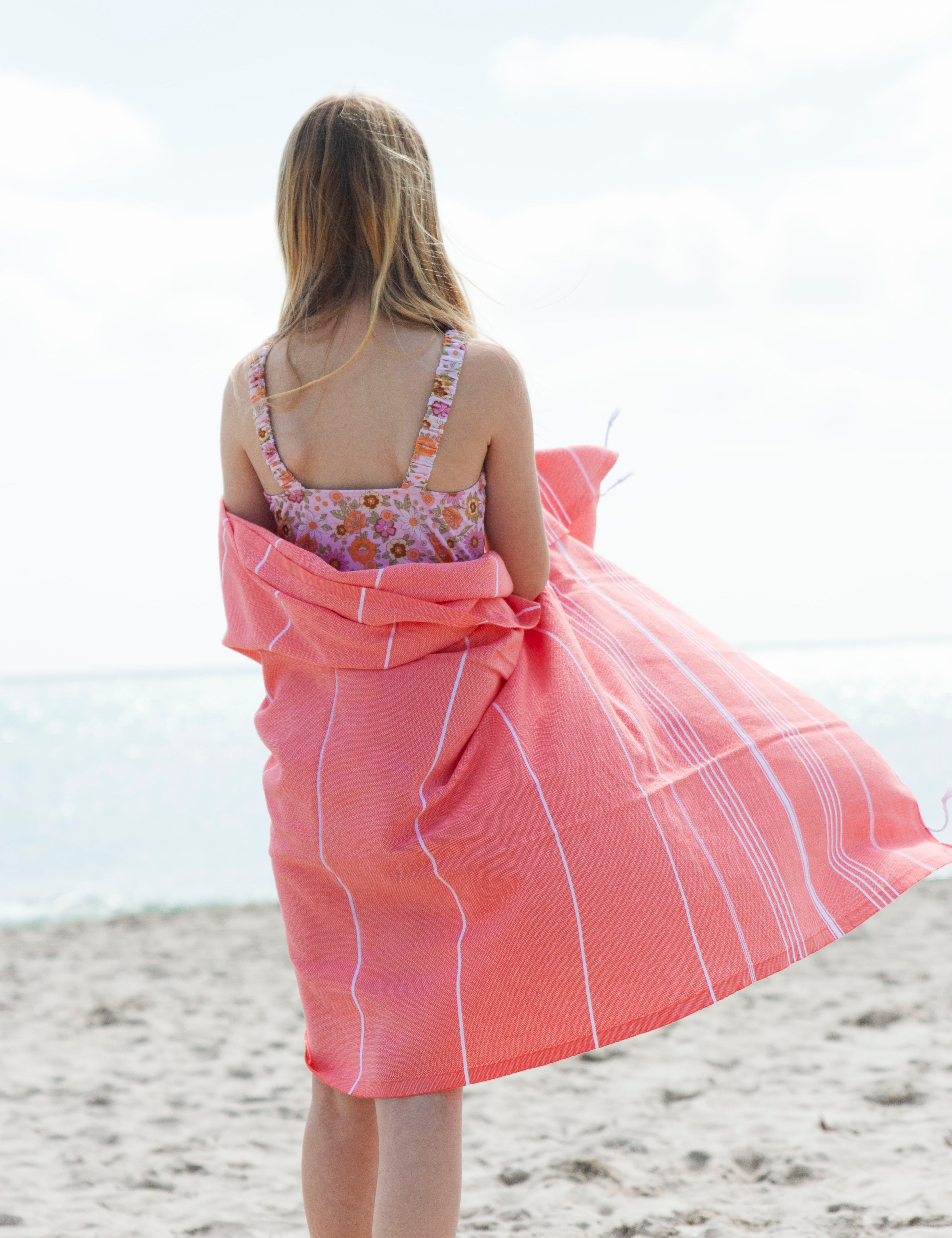  A girl on a beach wrapped in a coral Classic Turkish Towel