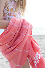 A close up of the Classic Coral Turkish towel wrapped around a girl wearing a floral bathing suit on the beach