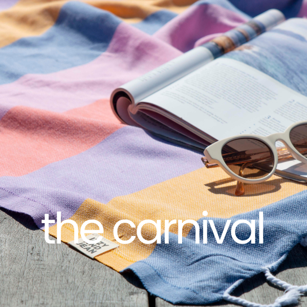 Colorful striped towel with a book and sunglasses on top, branded 'the carnival'.