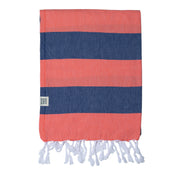 A folded santorini Turkish Towel in Navy and Coral large stripes, with white tassels at the end on a white background
