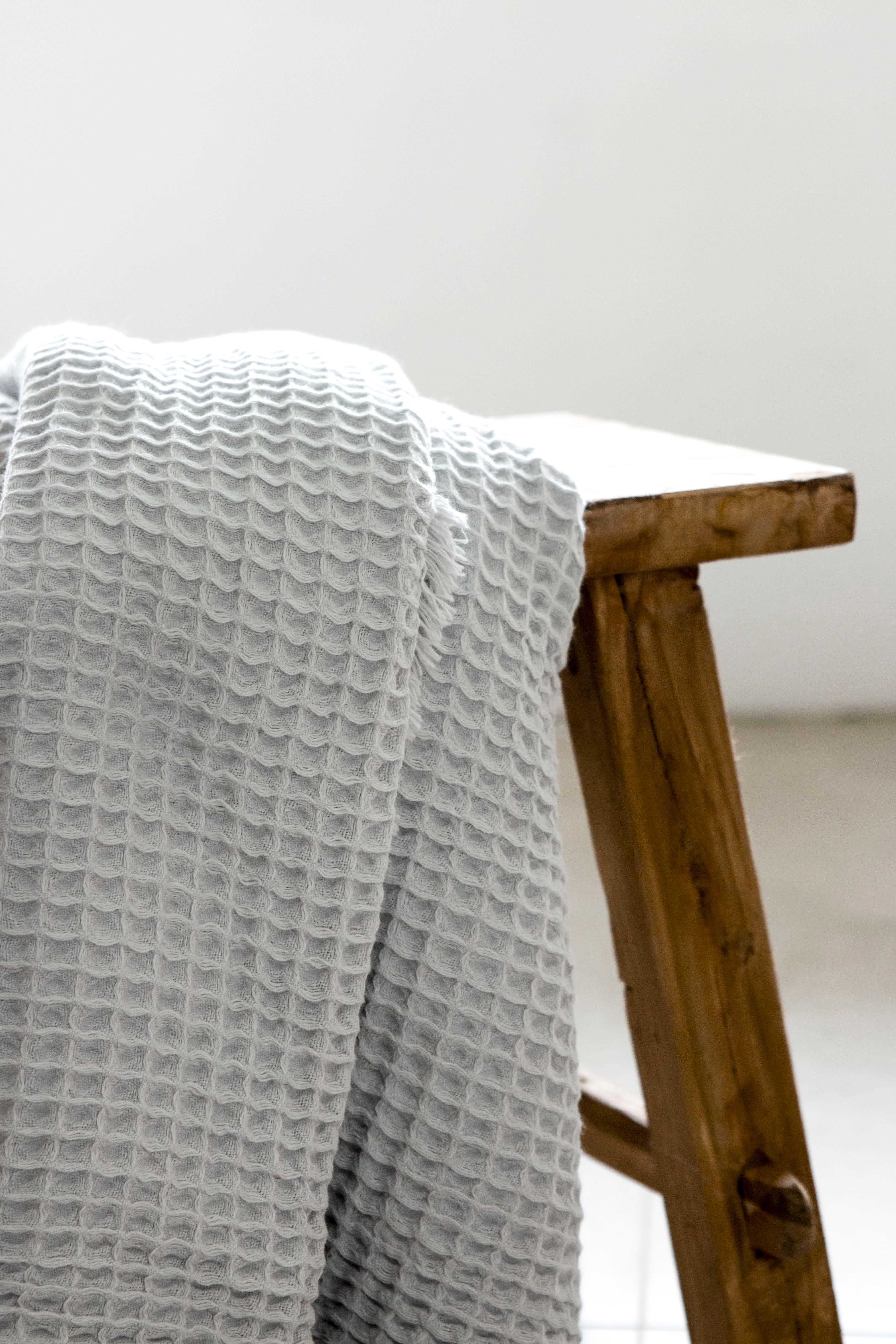 A pale grey waffle bath towel hanging on a wooden stool.