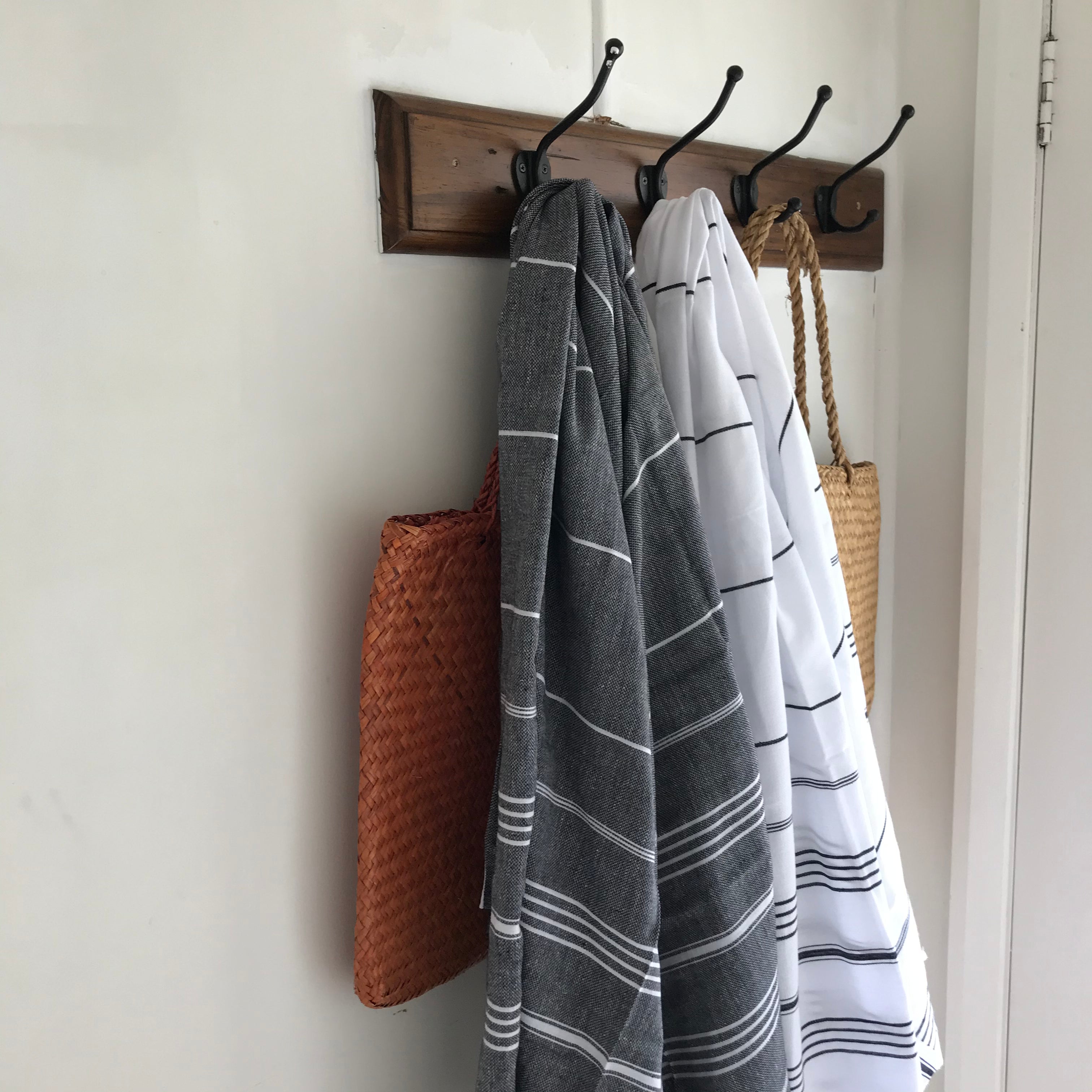 A white Turkish towel with black stripes and tassels on the bottom edge hangs on a hook next to a black Turkish Towel with white stripes