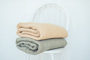 the mustard and sage coloured bed and couch throw blankets folded on a while chair