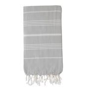 A folded pale grey Turkish towel with white stripes and tassels on the bottom edge.