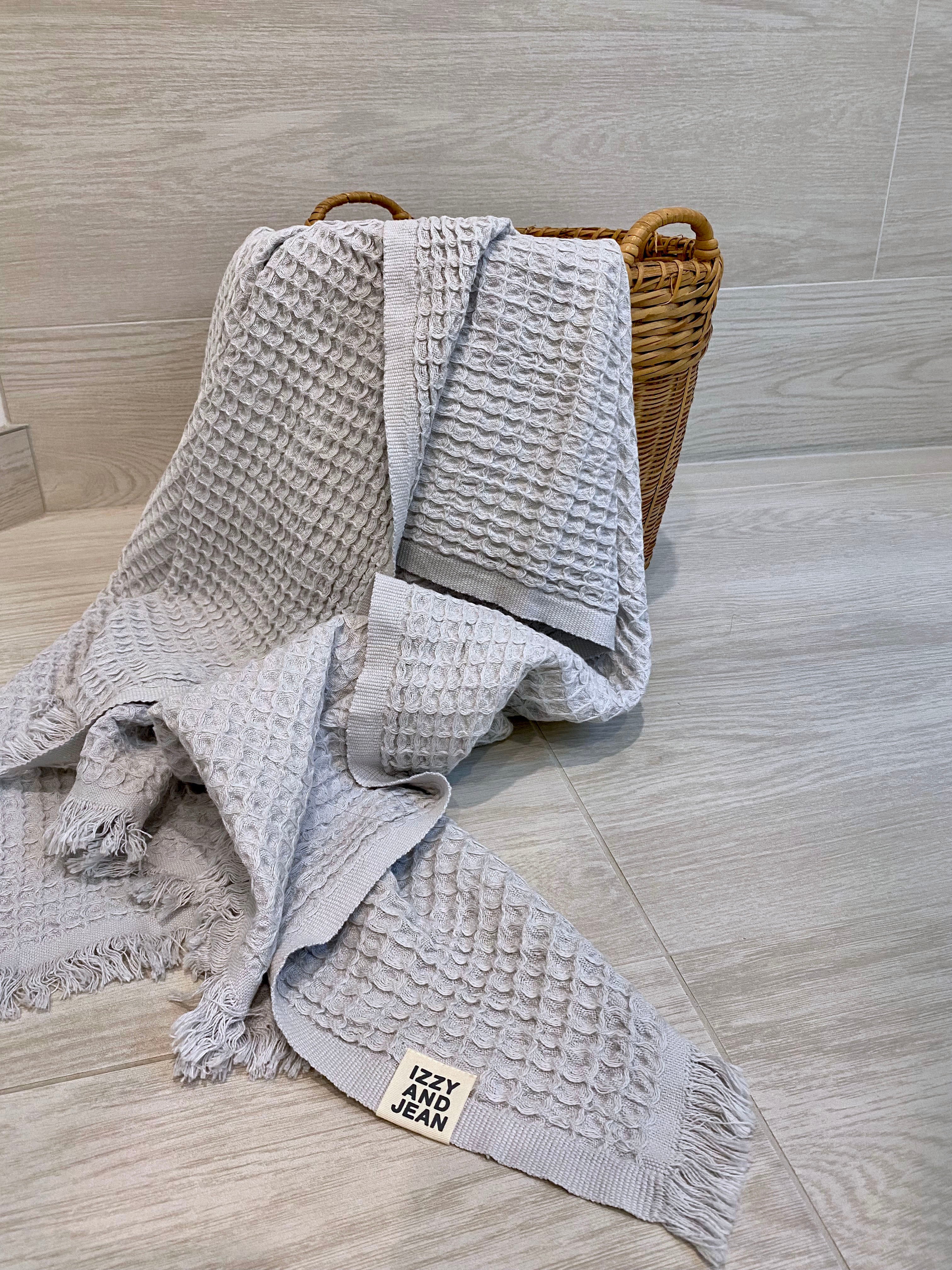 A pale grey waffle bath towel lying over a weave basket on a bathroom floor